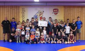 Die symbolische Scheckübergabe von Josef Frauenlob, Vorstand der Volksbank Raiffeisenbank Oberbayern Südost e.G., an Vereinsvorstand Max Stadler und den 2. Abteilungsvorstand der Ringer, Raymund Edfelder, im Beisein der Kinder und Trainer des Schülertrainings ((C) Maria Horn).